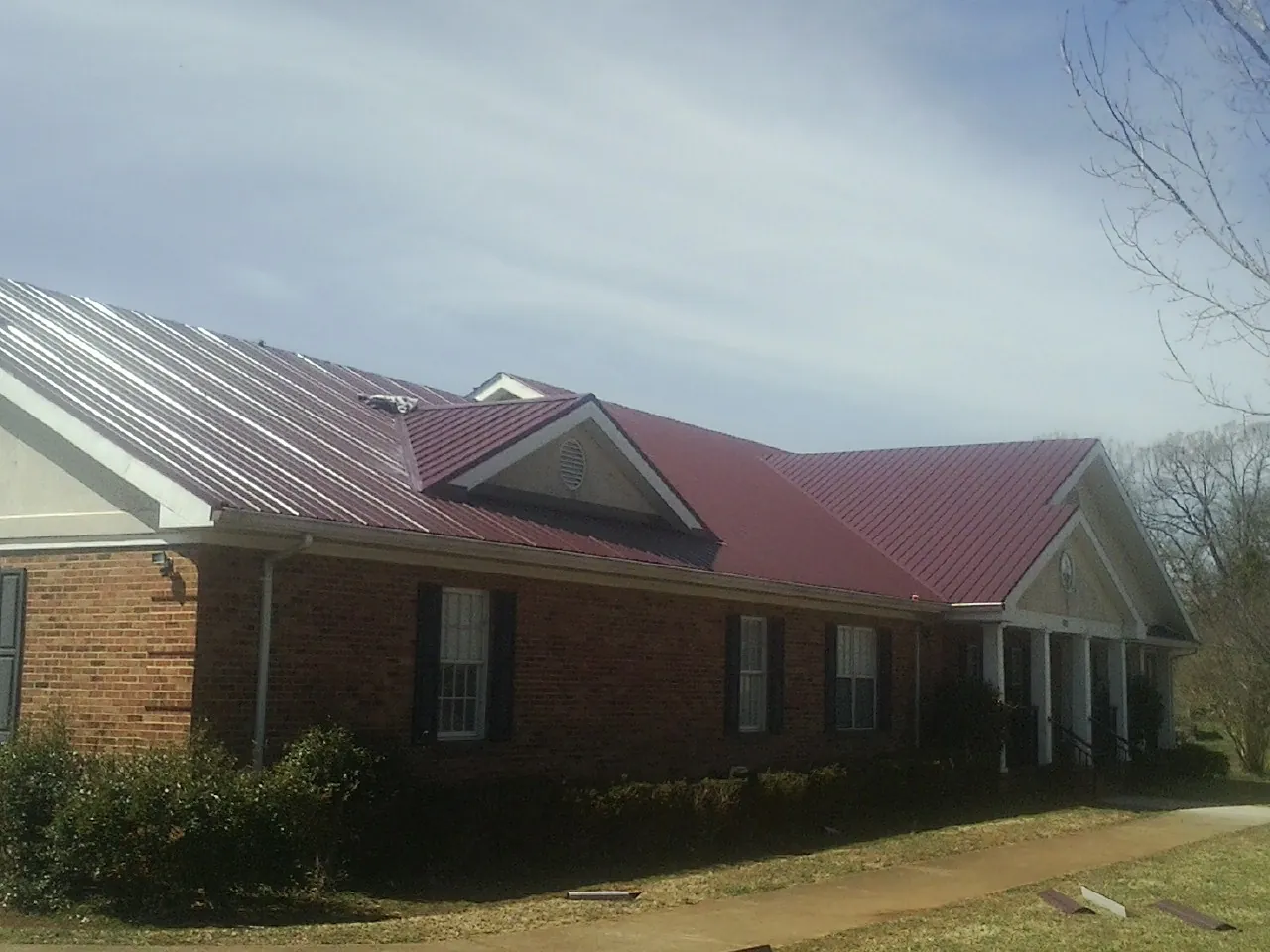 Red metal roof with gabled entries on a long brick building, from a Hail Damage Roof Repair job in Lore City