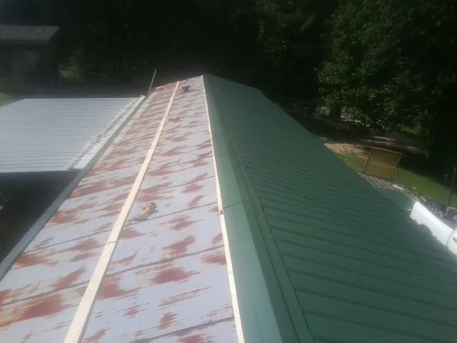 Old rusted panels beside newly installed green metal roofing — Wind Damage Roof Repair by Roofing Brothers in Lore City