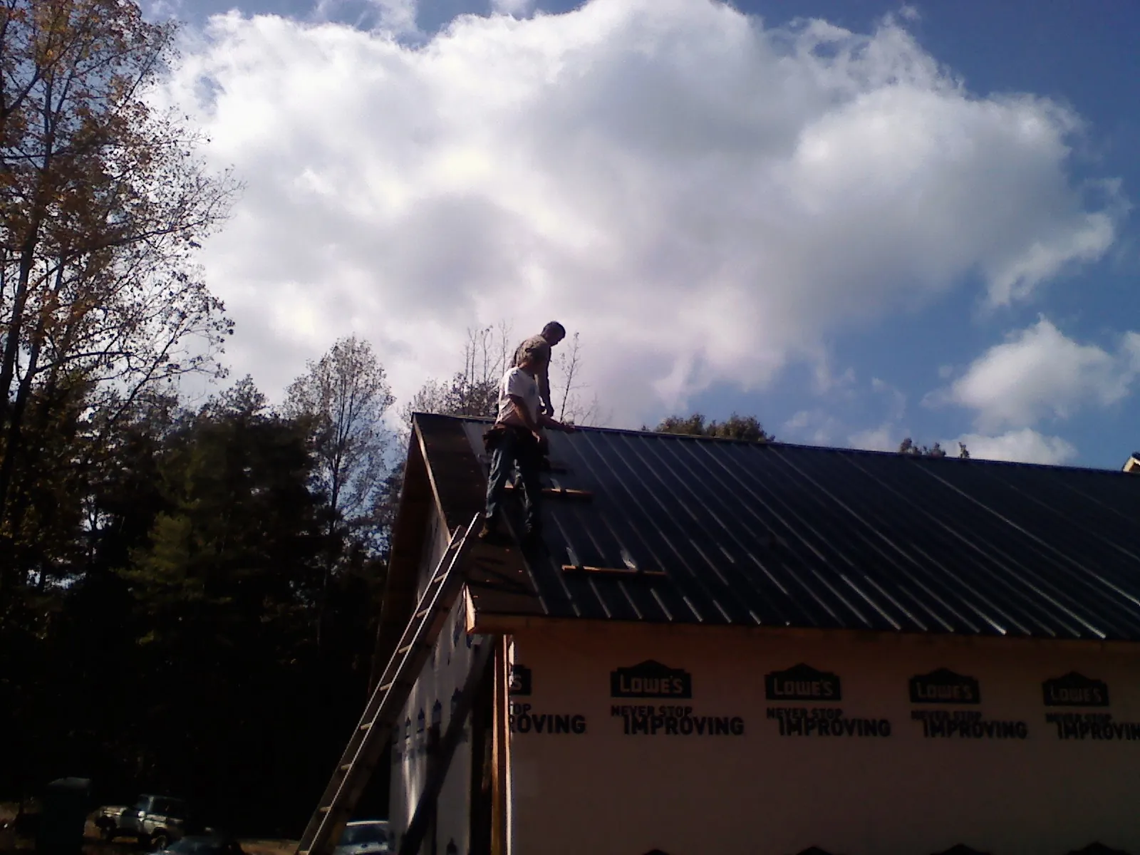 Roofer fastening dark metal panels high against a cloudy sky, from a Roof Inspection job in Lore City