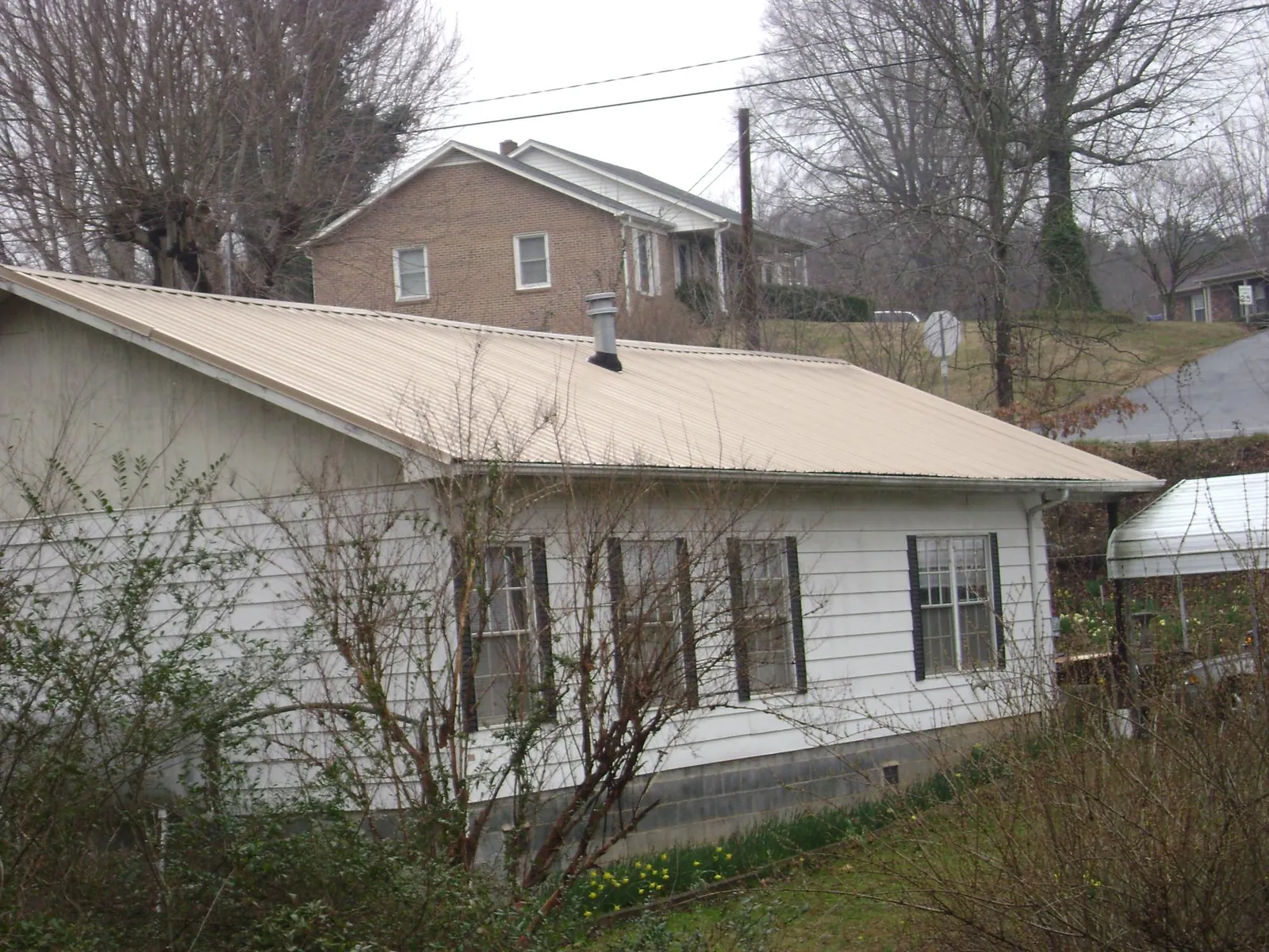 Tan metal roof on a white sided house set into a hillside — Commercial Roofing by Roofing Brothers in Lore City