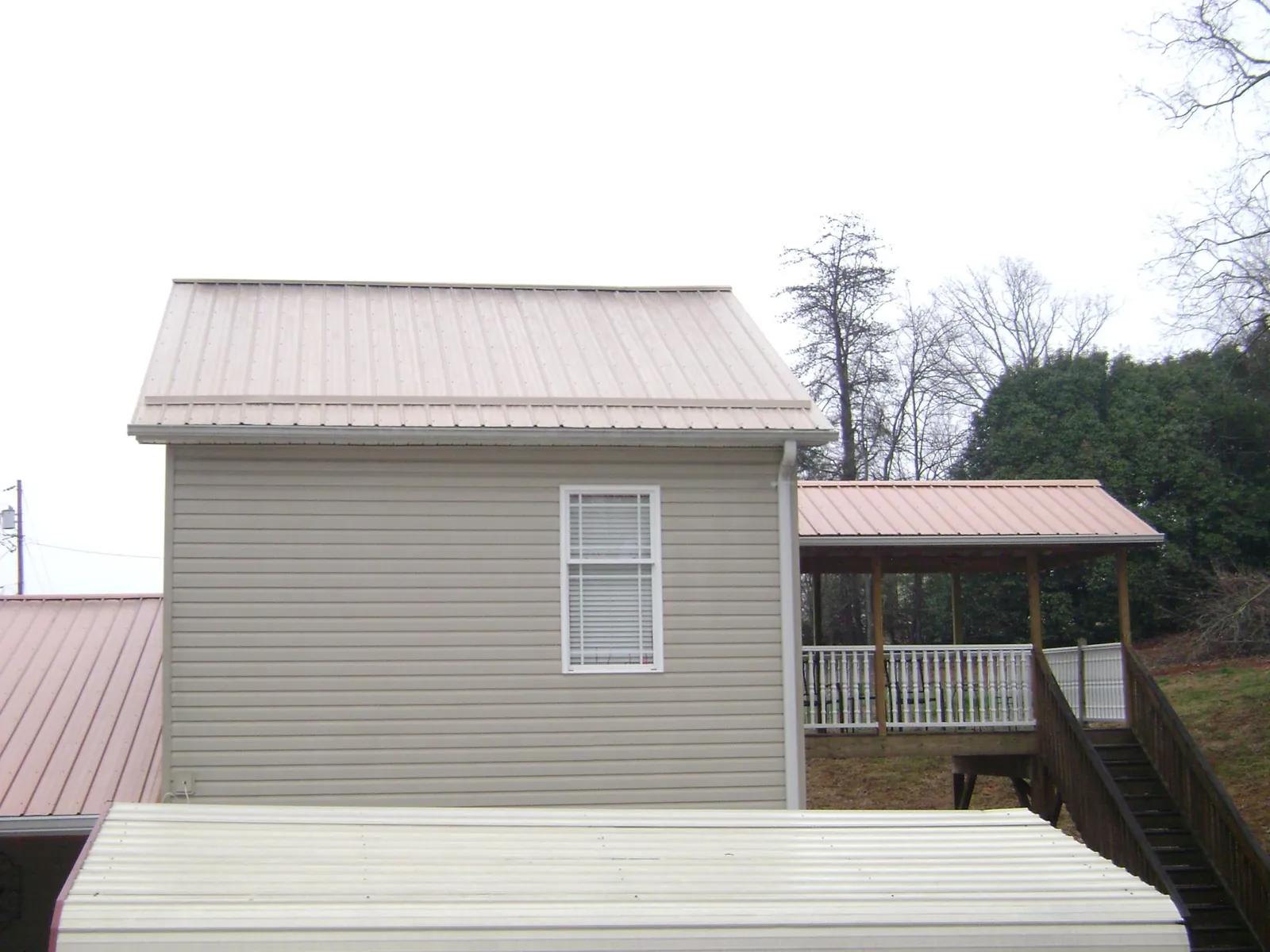 Tan metal roofs on a two story addition and attached porch, from a Roof Replacement job in Lore City
